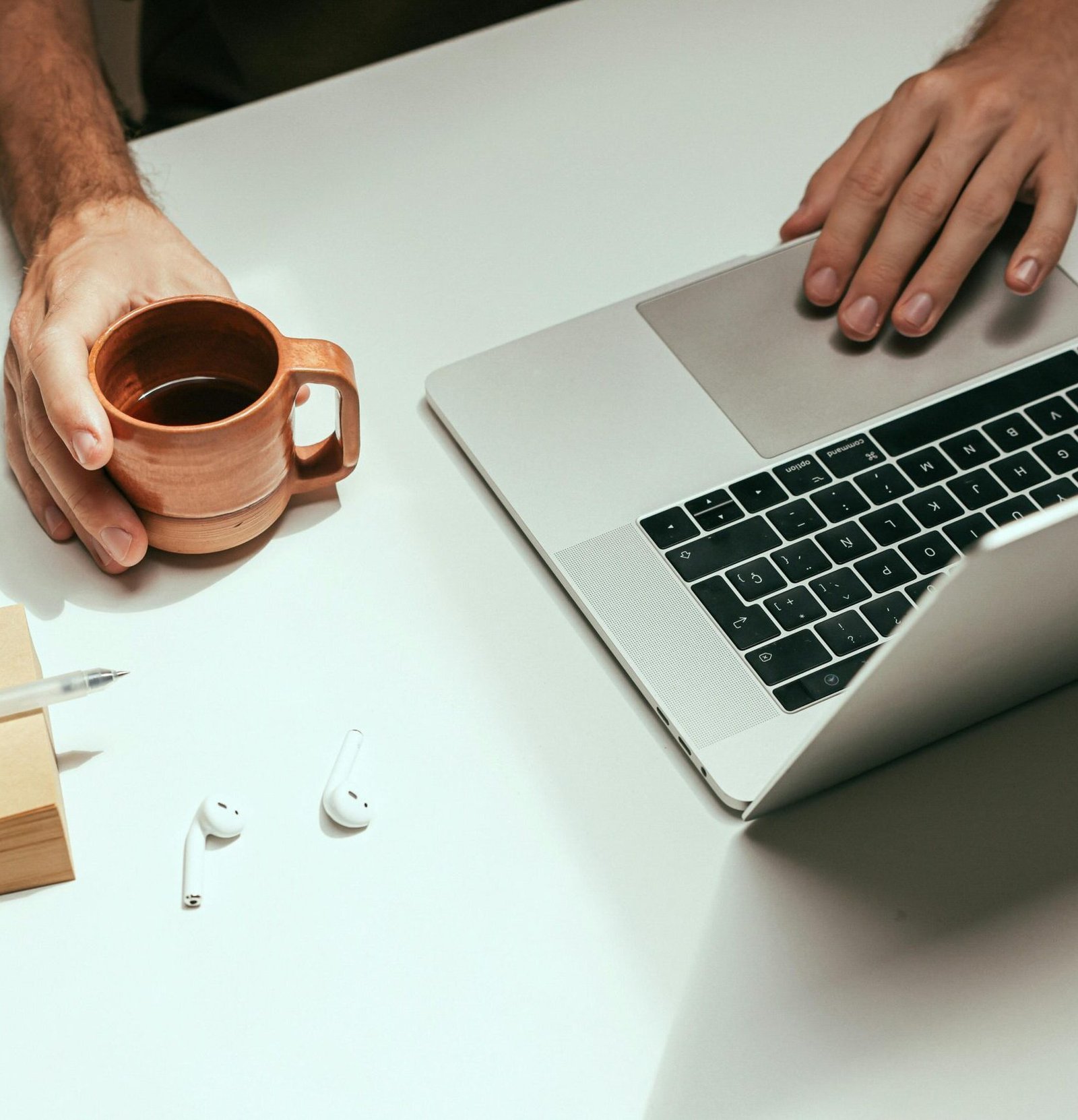 Minimalist workspace featuring a laptop, coffee mug, and AirPods for a modern work setup.
